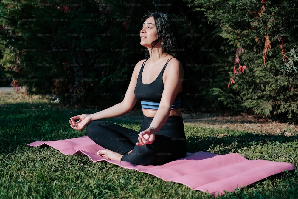 a woman sitting on a pink yoga mat in a park