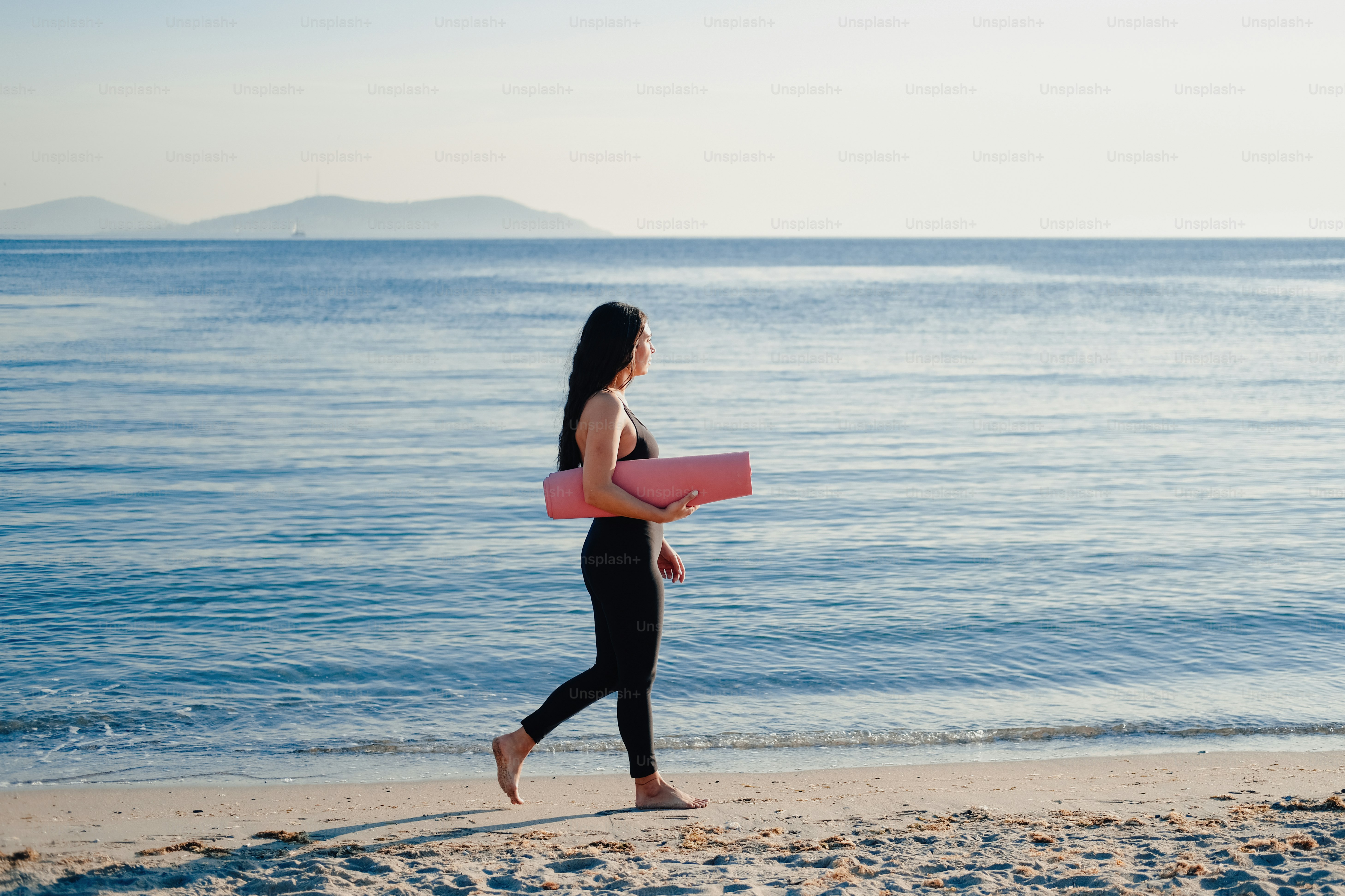 a woman walking on the beach carrying a surfboard