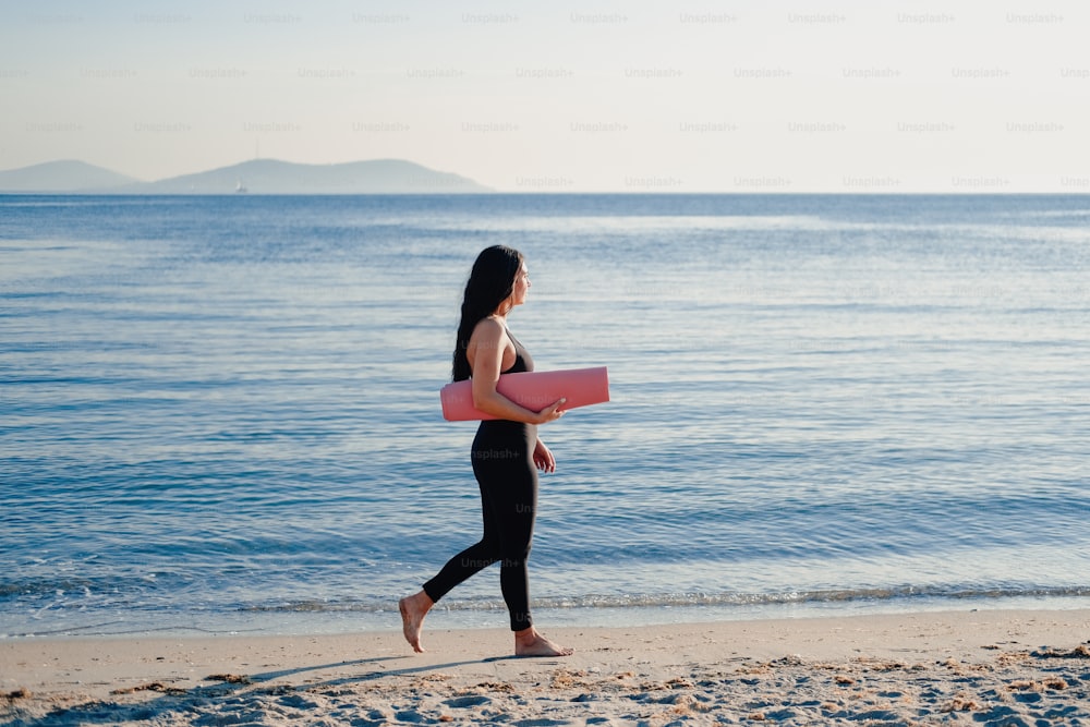 Una donna che cammina sulla spiaggia portando una tavola da surf