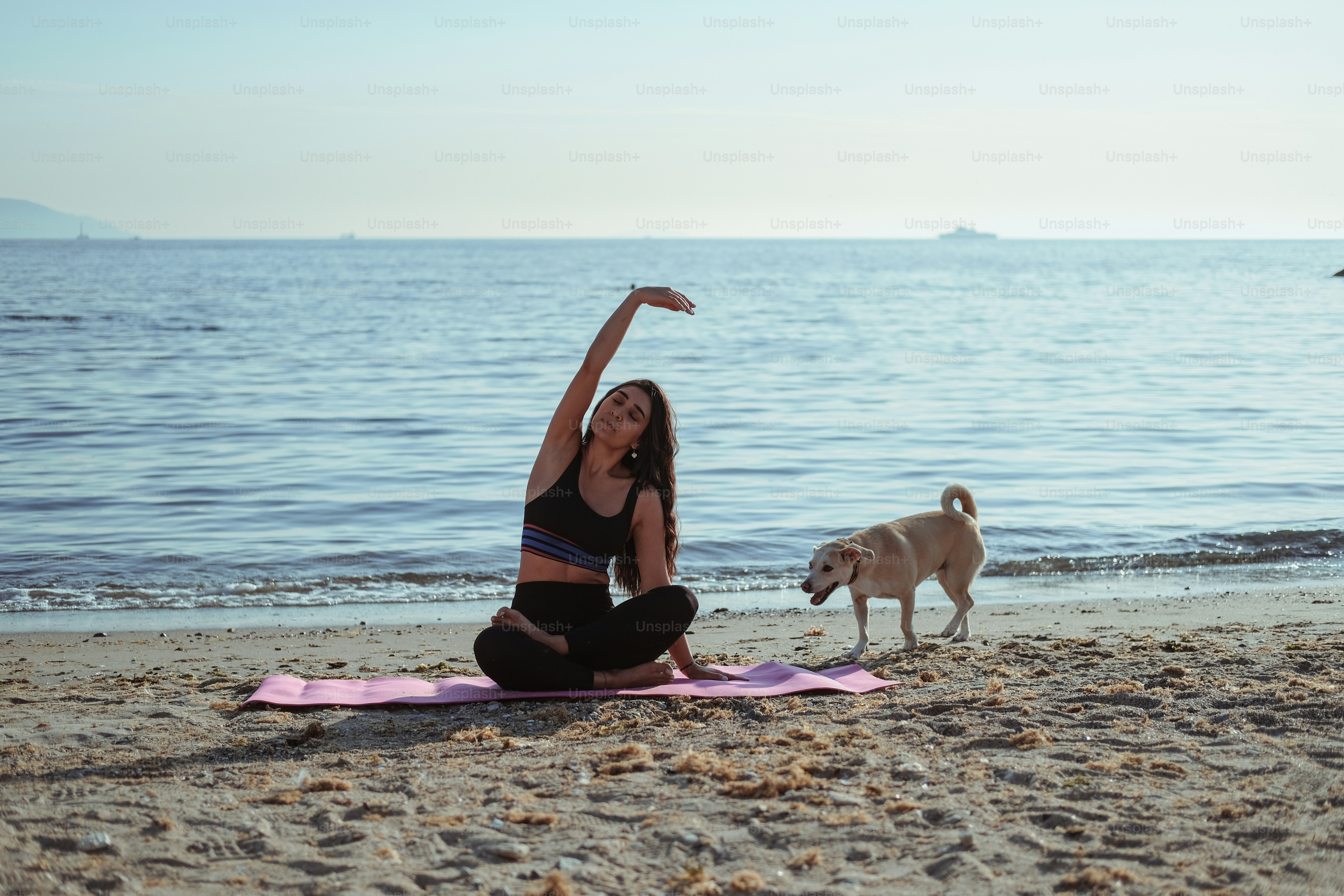 Eine Frau, die mit ihrem Hund Yoga am Strand macht