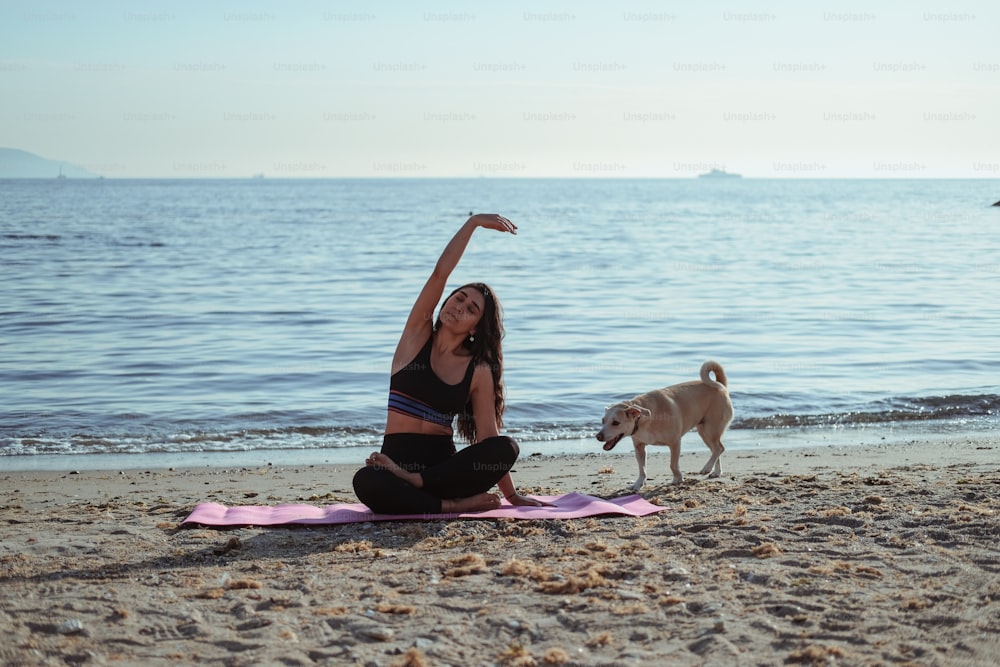 Eine Frau, die mit ihrem Hund Yoga am Strand macht