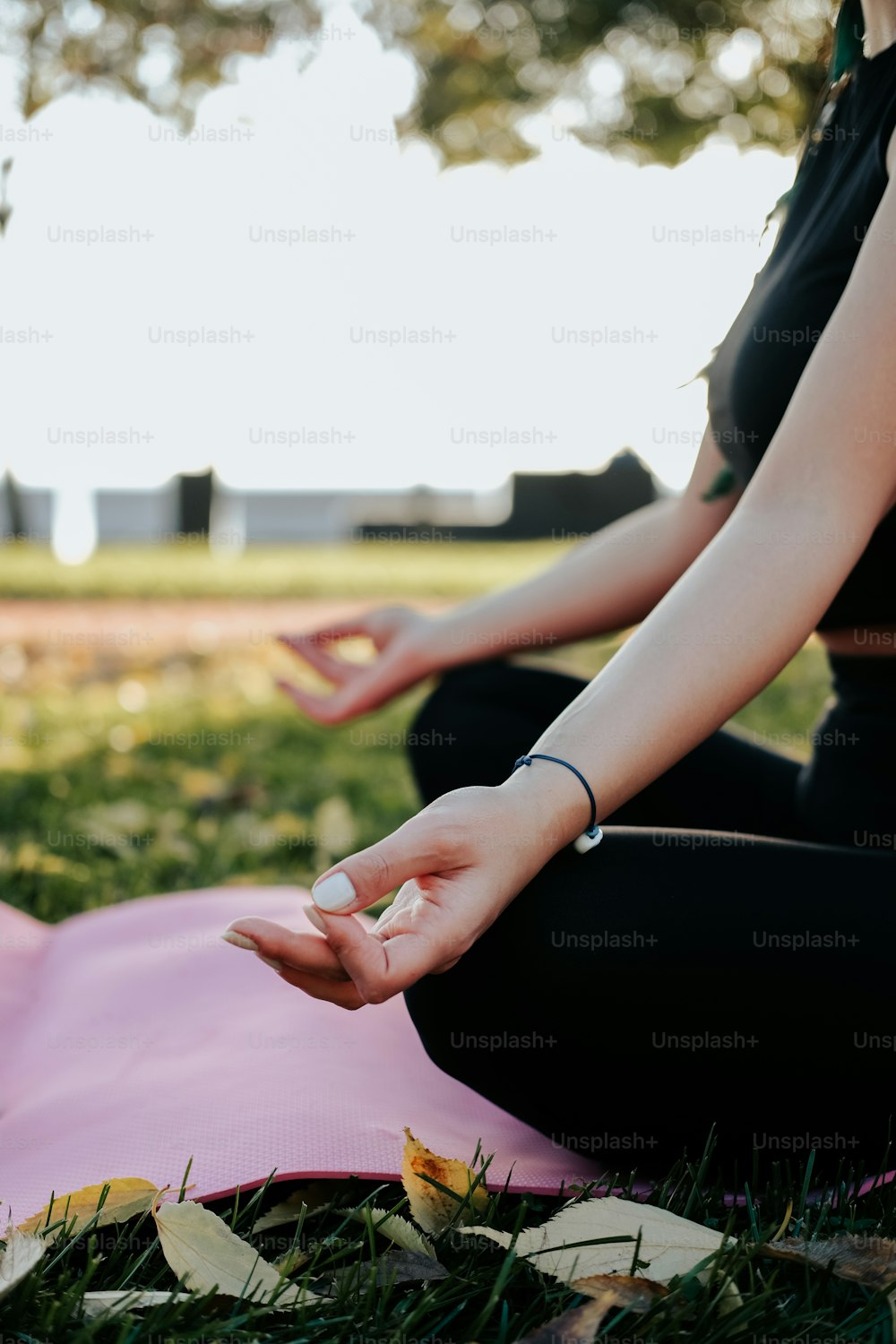 a woman sitting on a pink yoga mat in a park