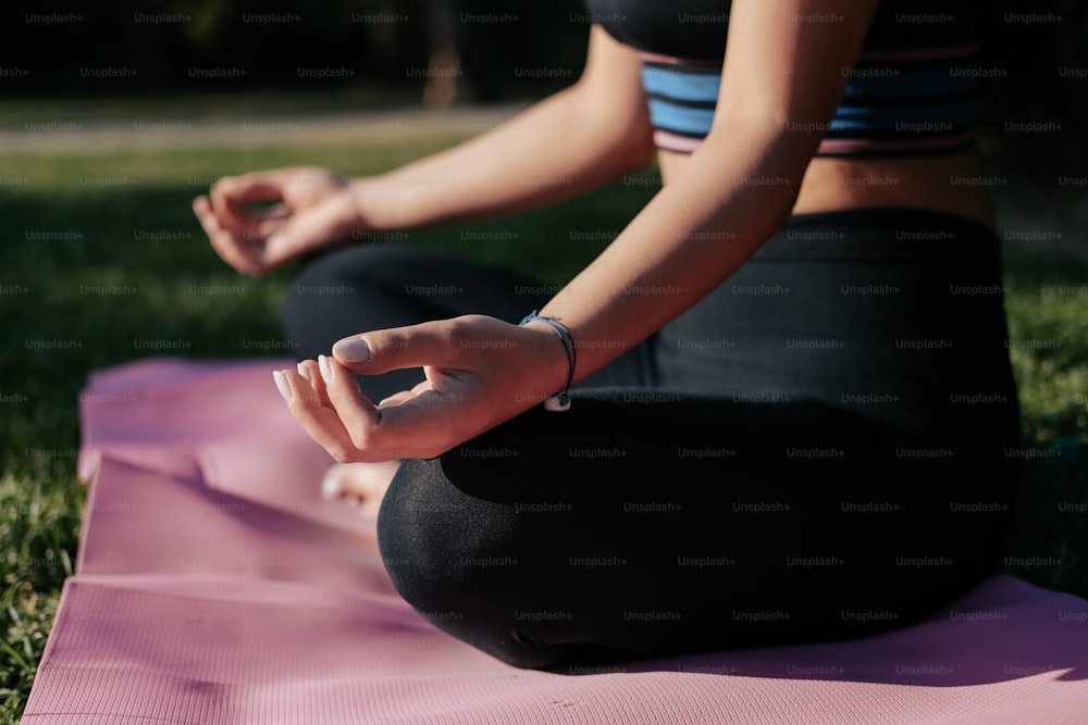 a woman sitting in a yoga position on a pink mat
