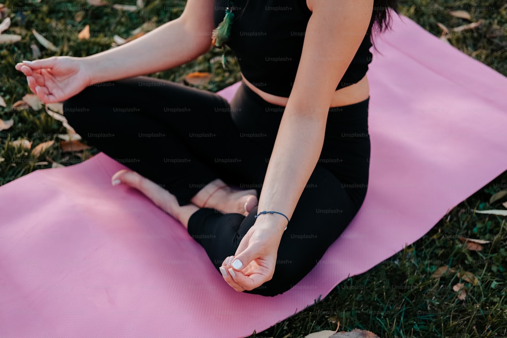 eine frau, die auf einer rosa yogamatte im gras sitzt