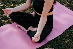 a woman sitting on a pink yoga mat in the grass