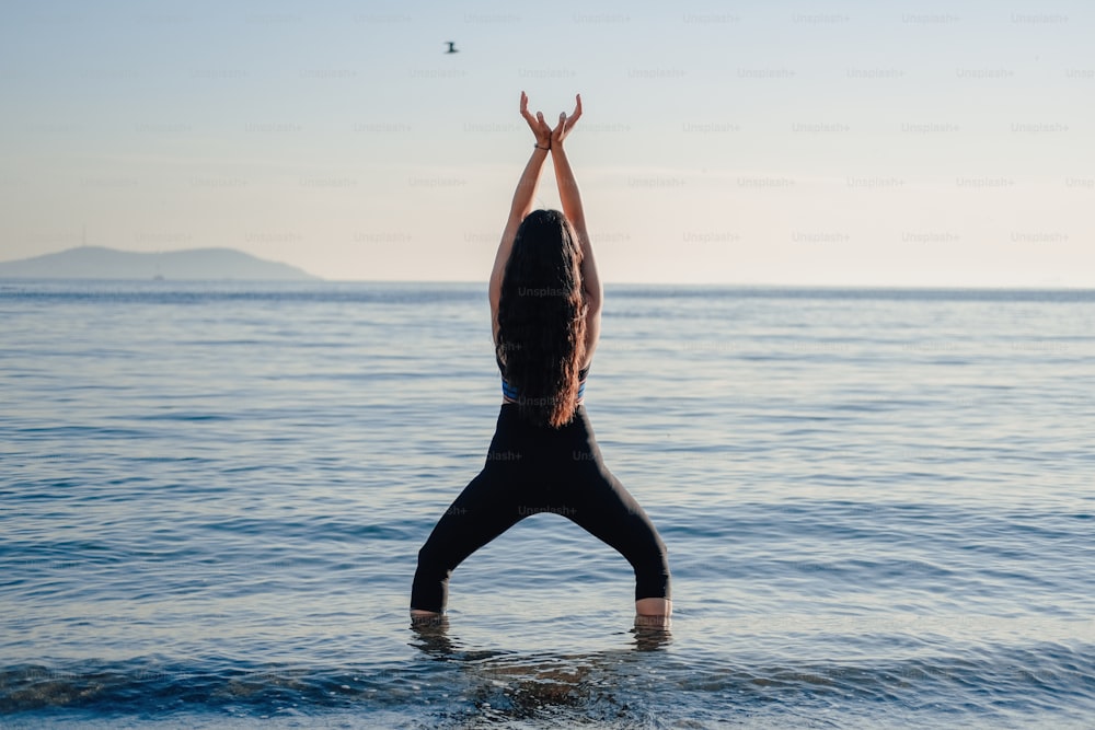 a woman standing in the ocean with her hands up