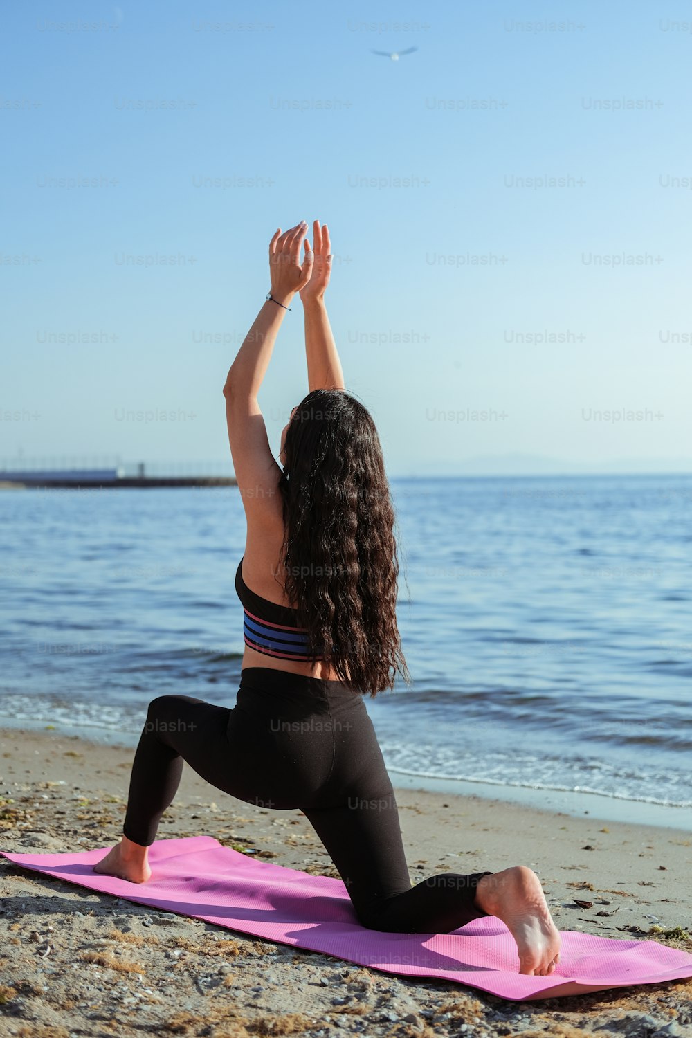 Una donna che fa yoga su un tappetino rosa sulla spiaggia