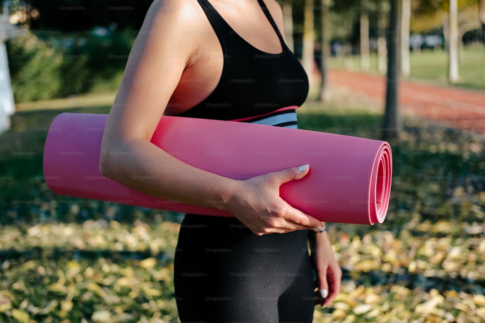 uma mulher segurando um tapete de yoga rosa em um parque