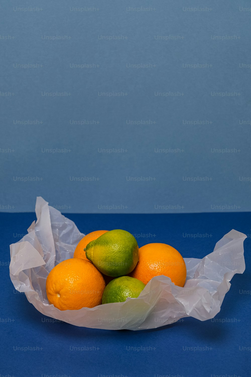 una ciotola piena di arance e lime in cima a un tavolo blu