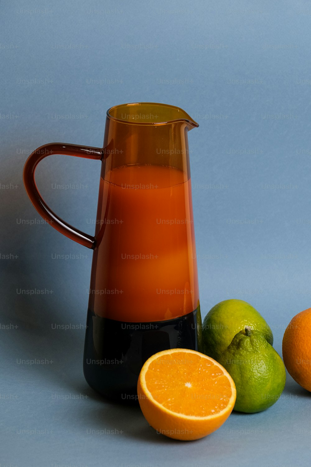 a pitcher of orange juice next to two limes and an orange