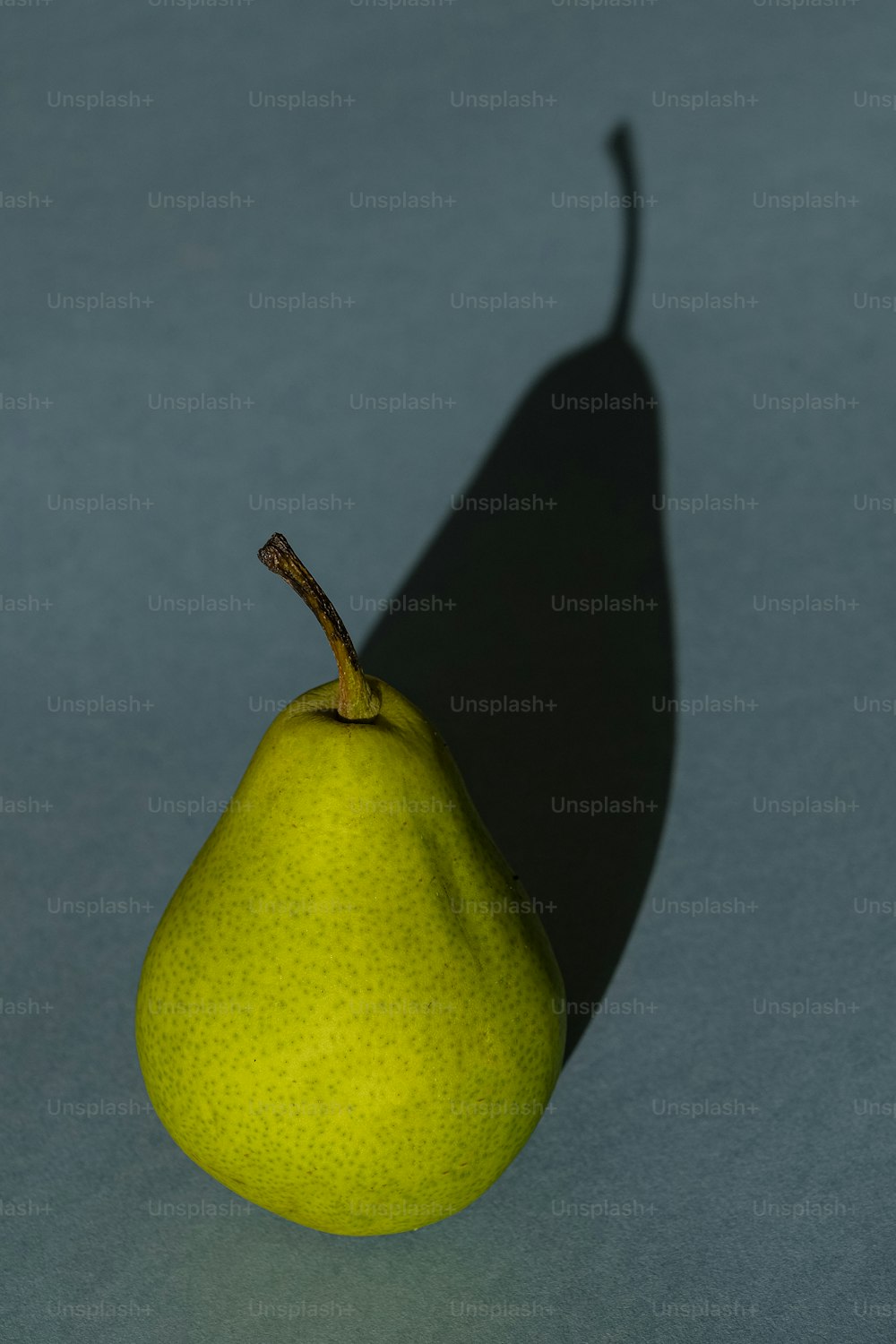 a single pear is casting a shadow on a blue surface