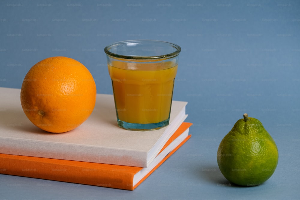 ein Glas Orangensaft neben einer Orange und einem Buch