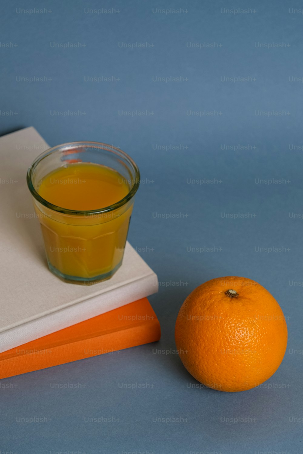 a glass of orange juice next to a stack of books