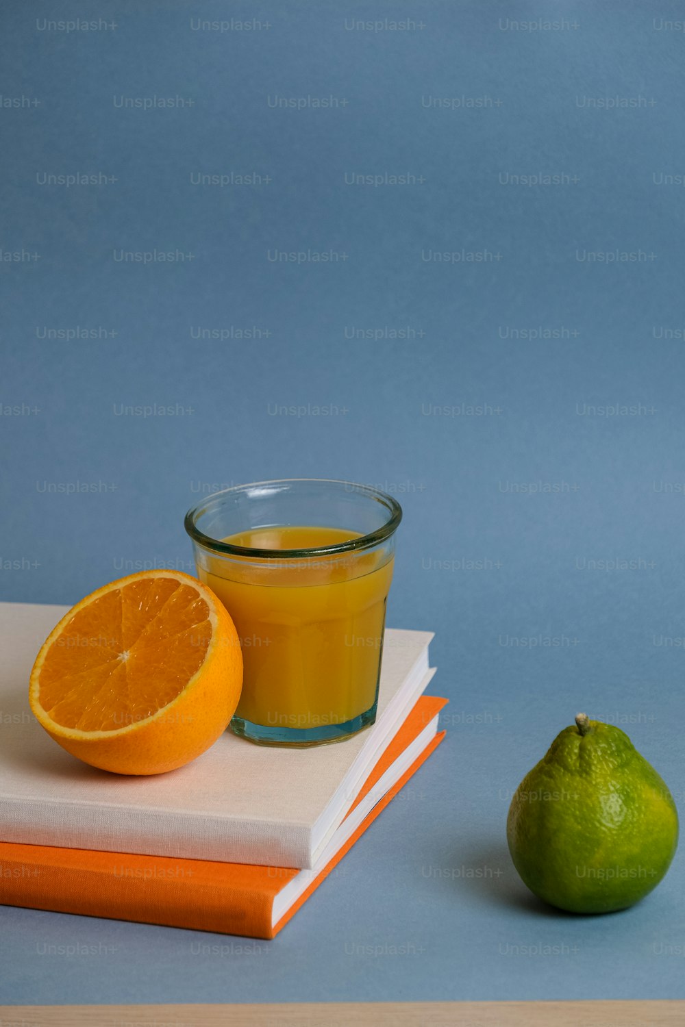a glass of orange juice next to a stack of books