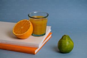 a glass of orange juice next to an orange and a book