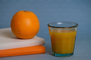 本の山の横にあるオレンジジュースのグラス