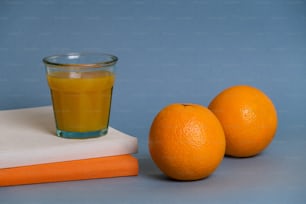 two oranges next to a glass of orange juice