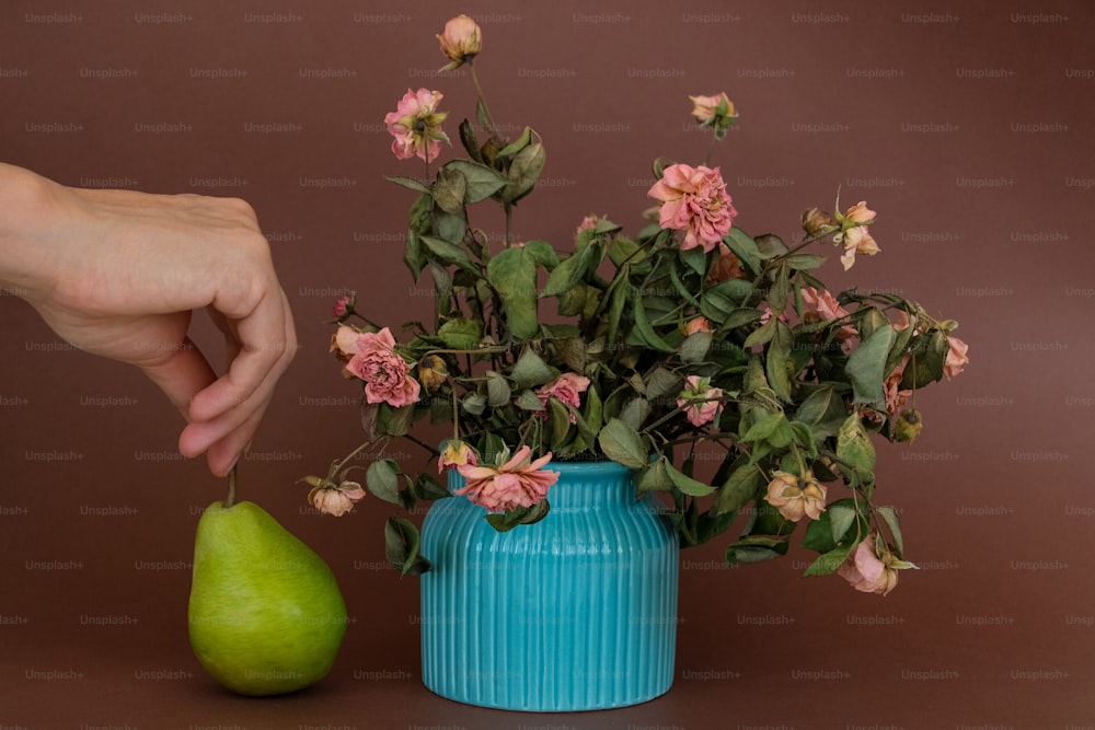 un vase bleu rempli de fleurs roses à côté d’une poire verte
