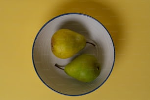 duas peras em uma tigela branca em uma superfície amarela