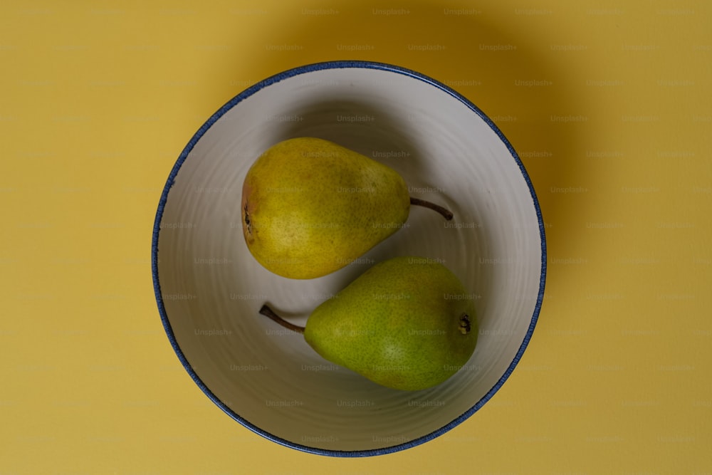 two pears in a white bowl on a yellow surface