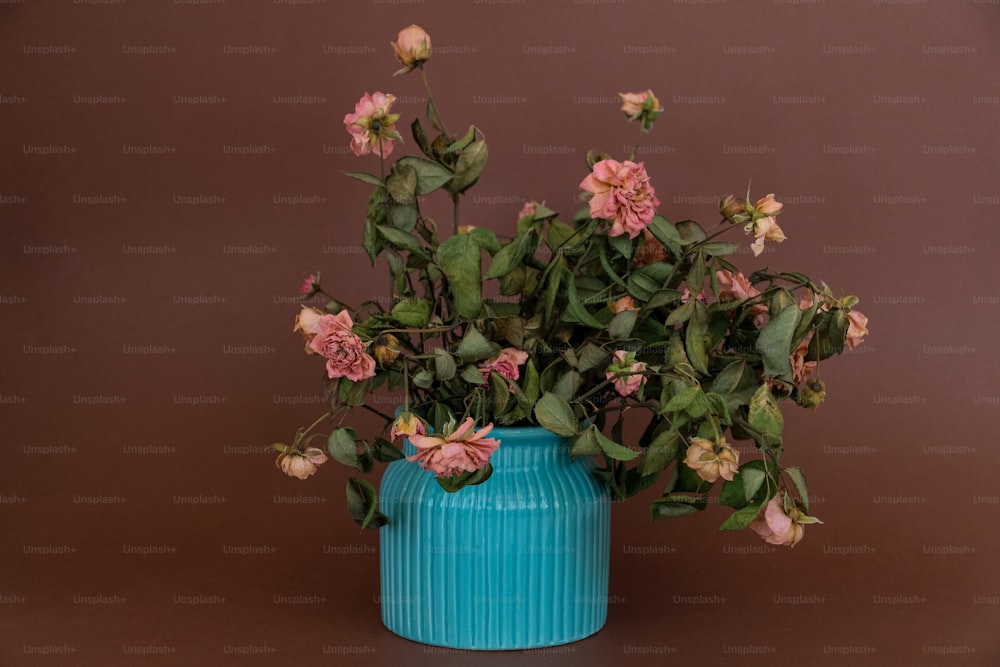 um vaso azul cheio de flores cor-de-rosa em cima de uma mesa