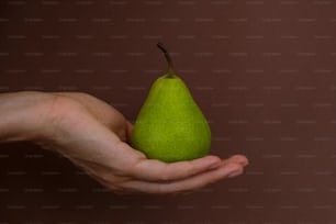 una persona che tiene una pera verde in mano