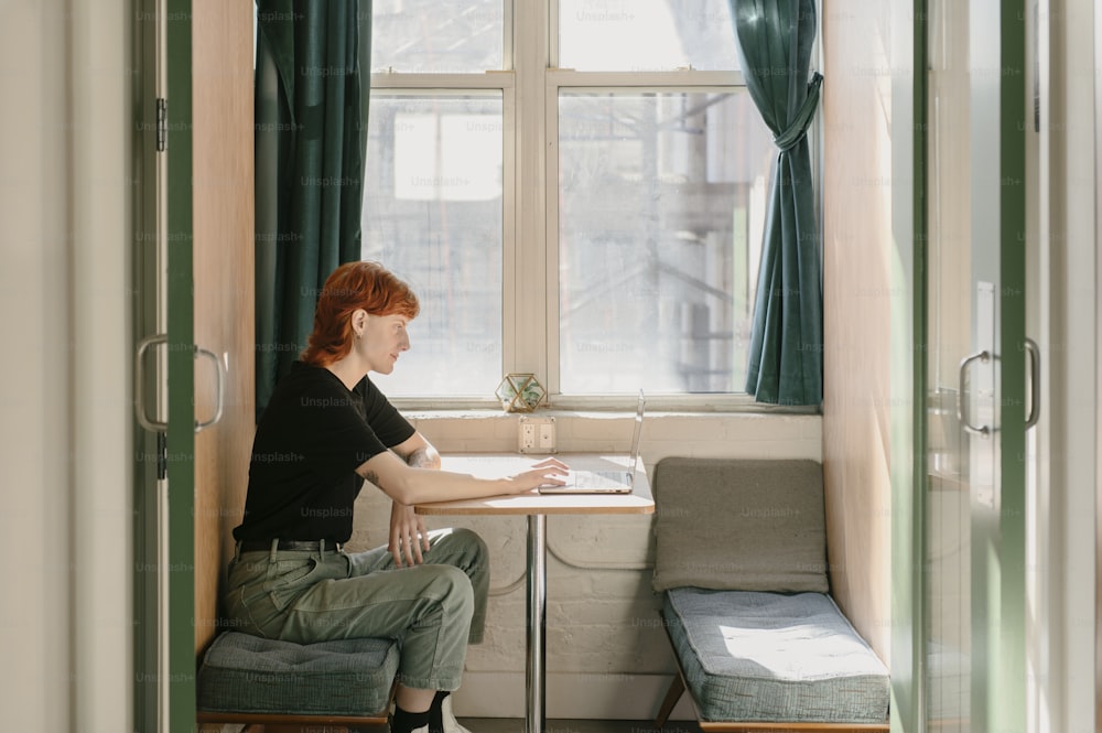 uma mulher sentada em uma mesa em frente a uma janela