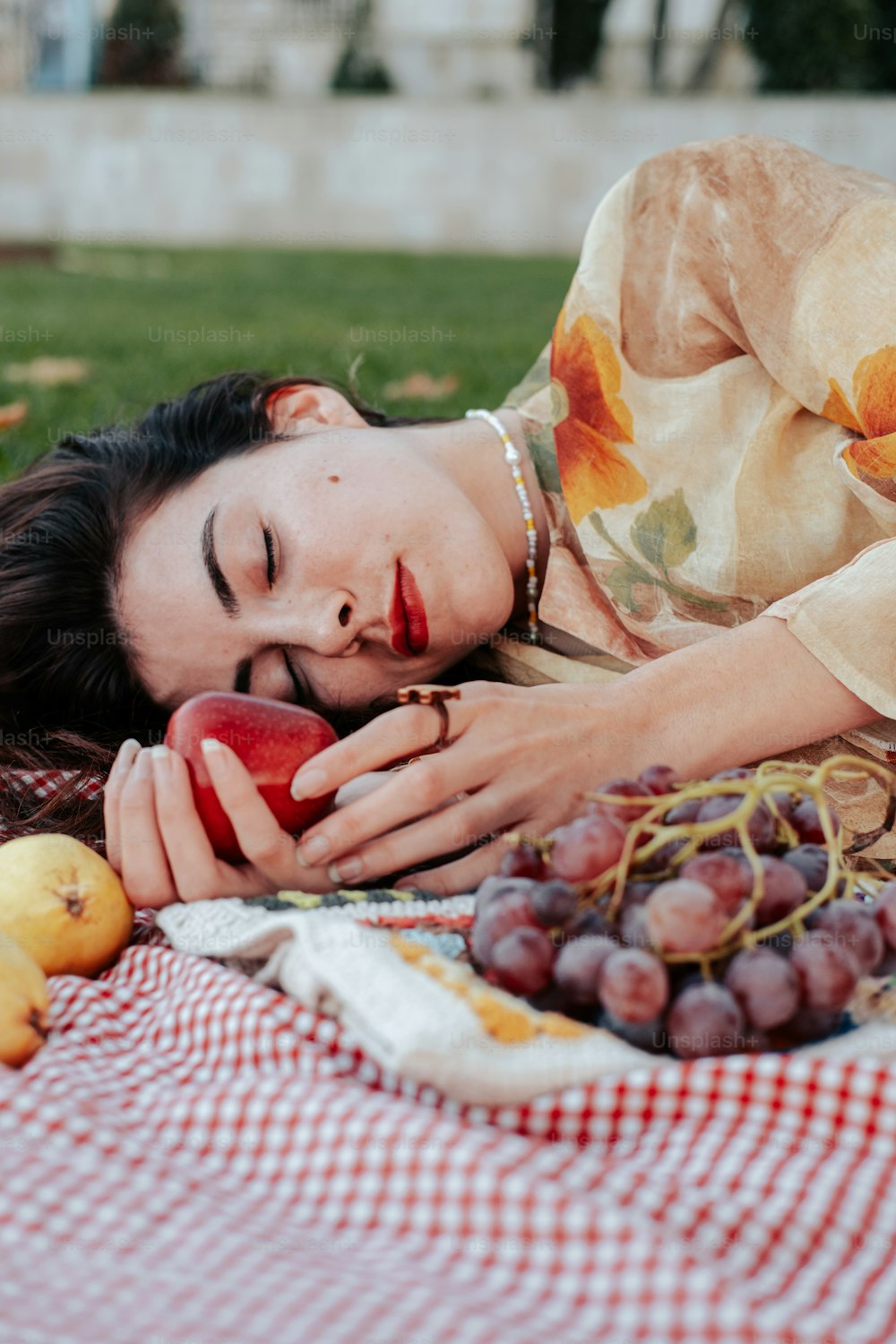 a woman laying on a blanket with grapes and apples