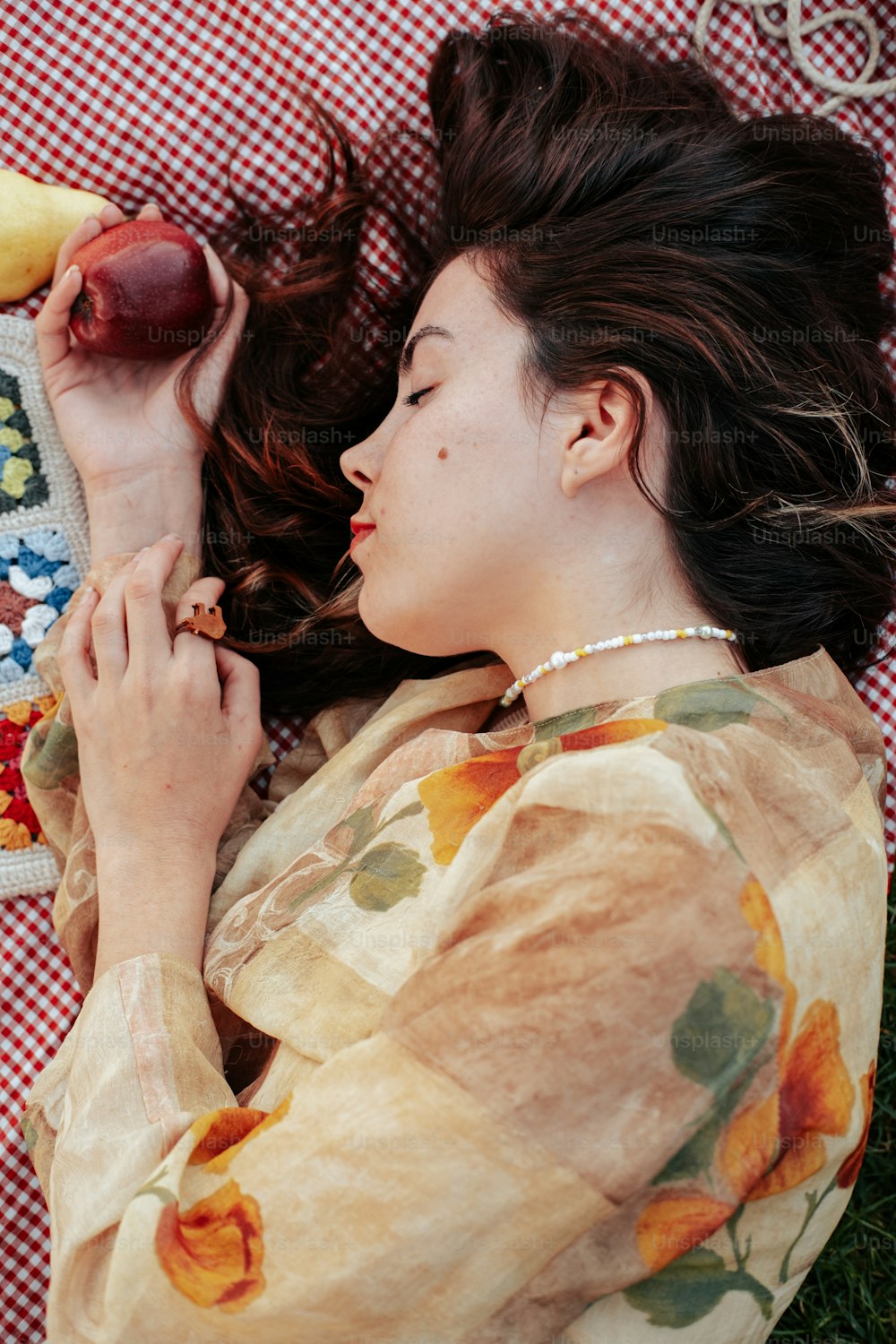 a woman laying on a blanket holding a banana and an apple