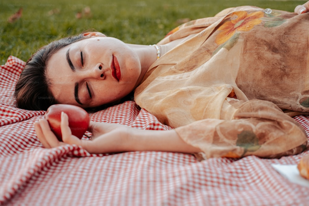 a woman laying on a blanket holding an apple