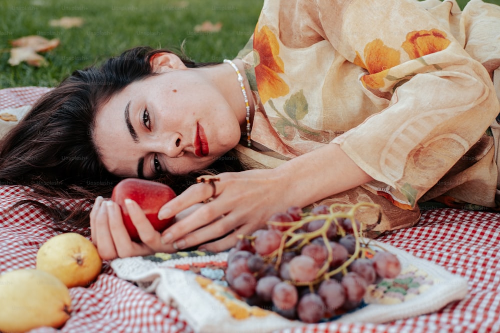 uma mulher deitada em um cobertor com um prato de frutas
