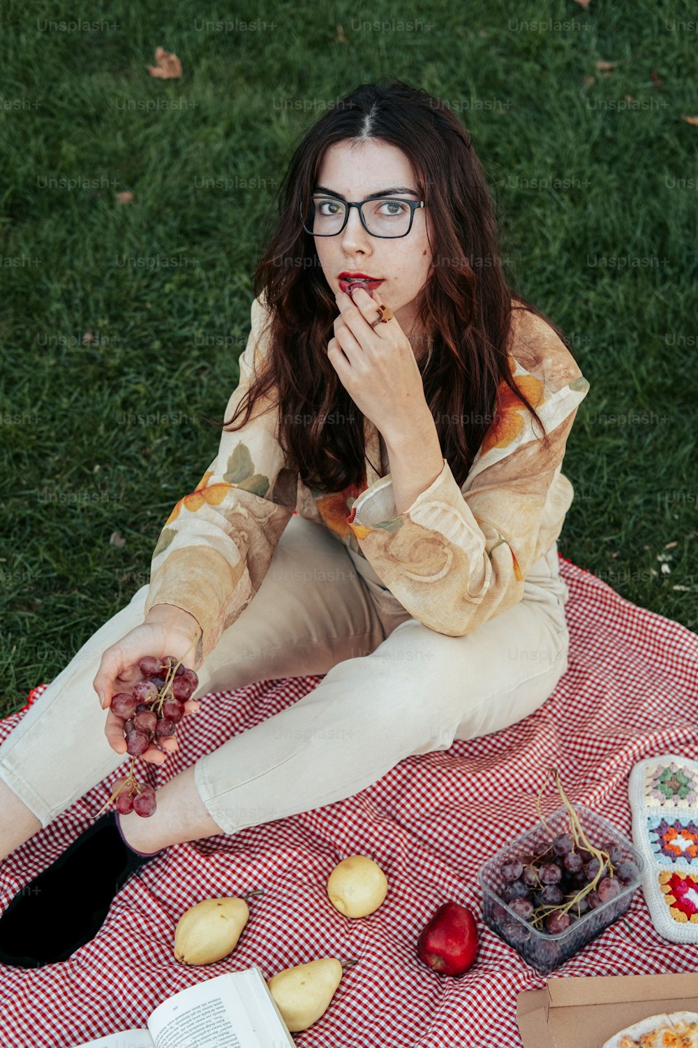 a woman sitting on a blanket eating grapes