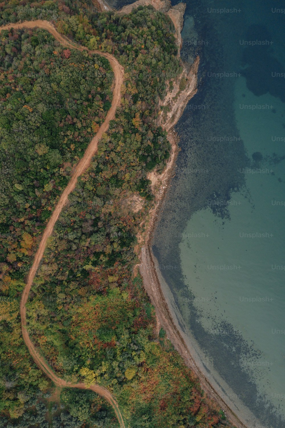 an aerial view of a winding dirt road next to a body of water