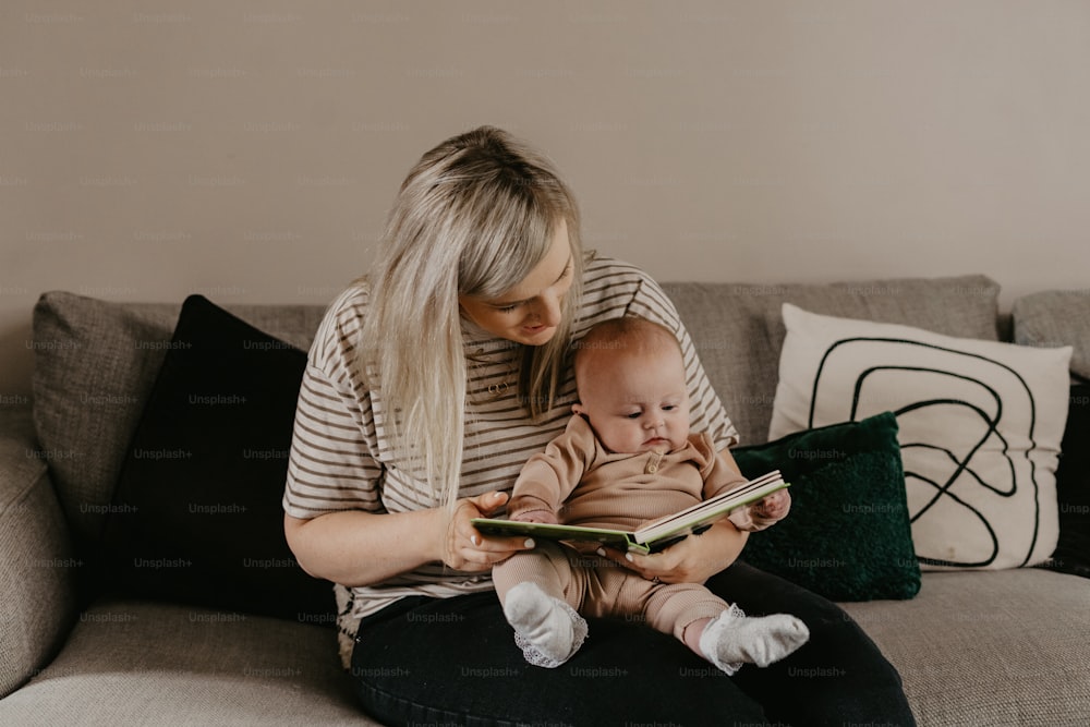 a woman sitting on a couch reading a book to a baby
