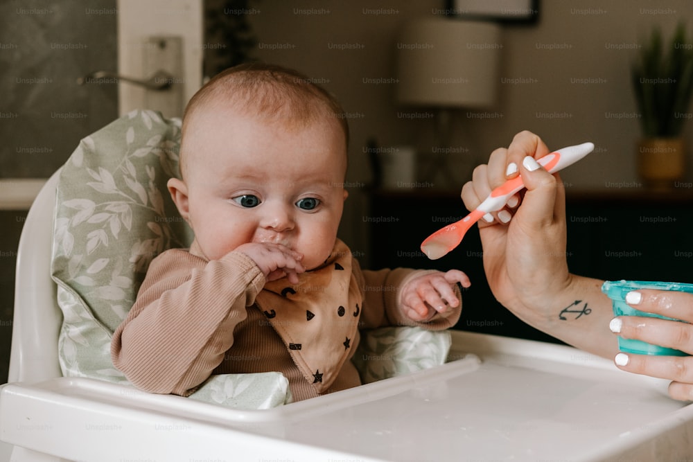 a baby in a high chair being fed with a toothbrush