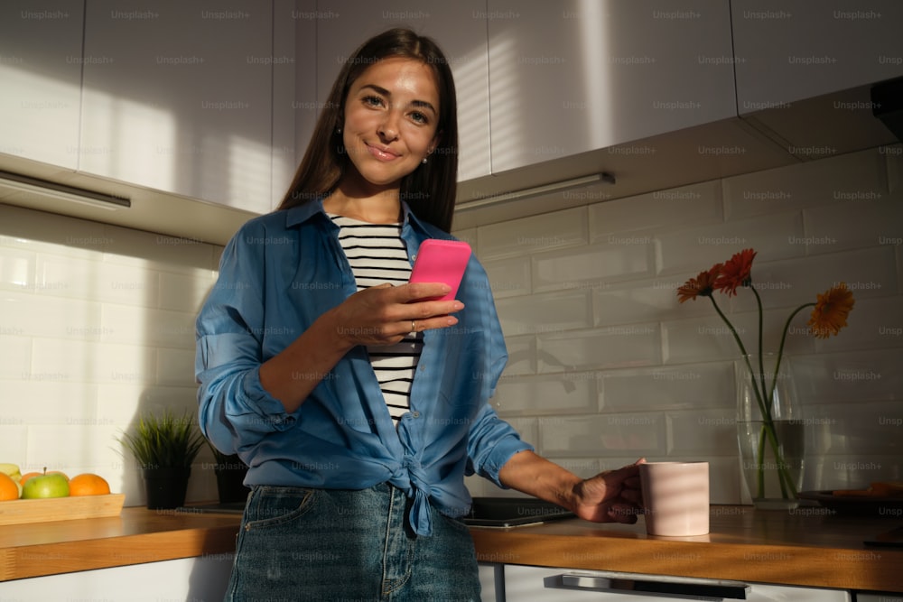 a woman standing in a kitchen holding a cell phone