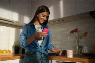 Una mujer parada en una cocina sosteniendo un teléfono celular