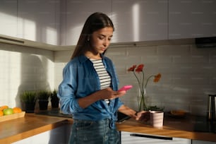 uma mulher em pé em uma cozinha olhando para um telefone celular