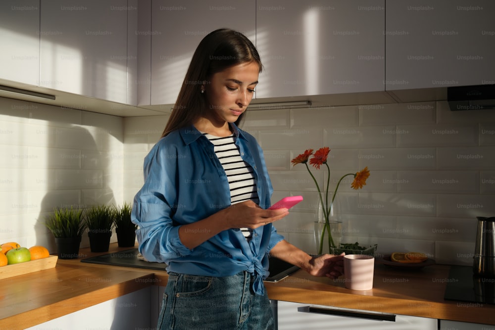 Une femme debout dans une cuisine regardant un téléphone portable