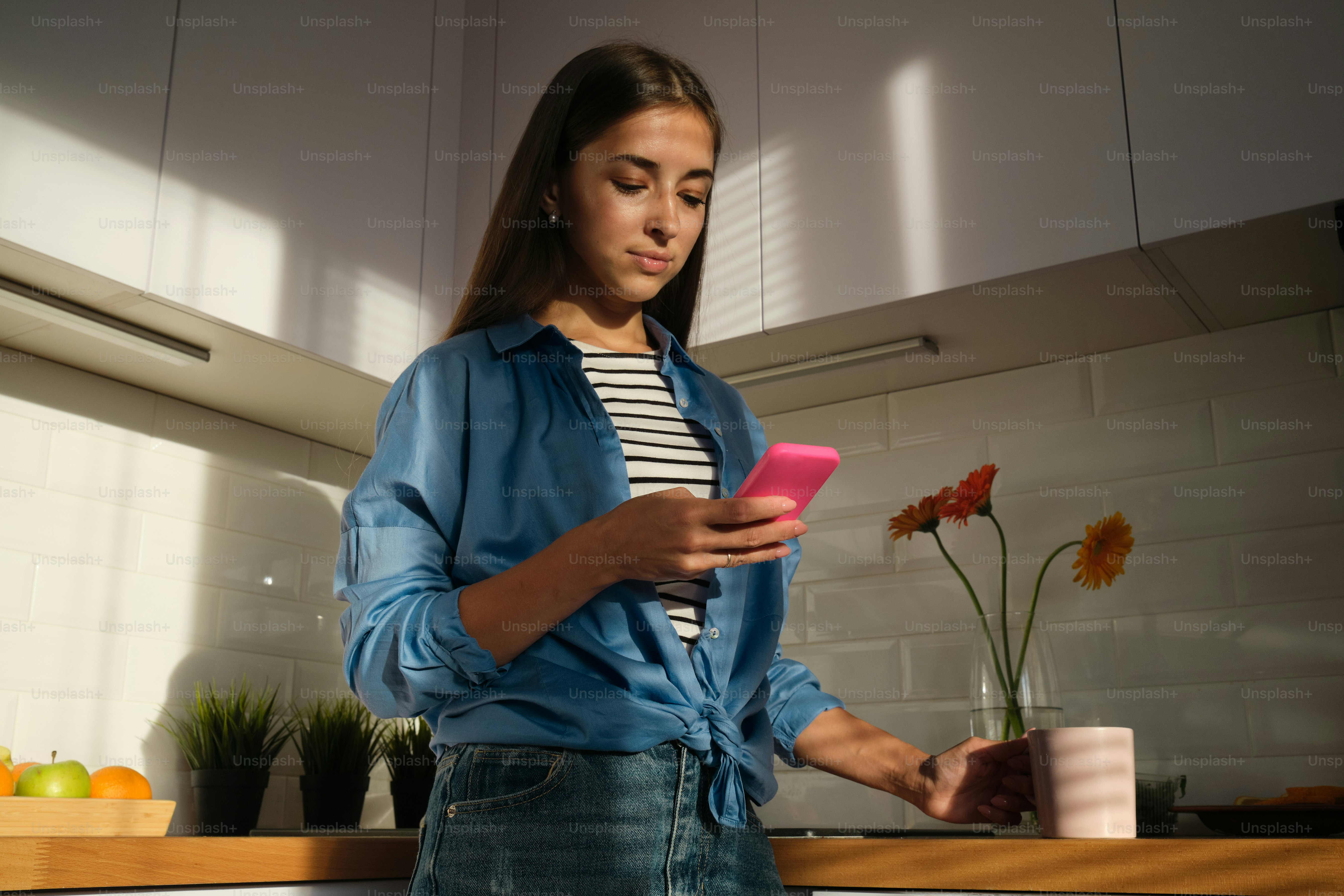 a woman standing in a kitchen looking at a cell phone