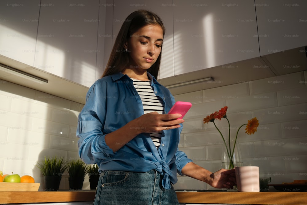 a woman standing in a kitchen looking at a cell phone