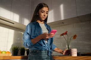 a woman standing in a kitchen looking at a cell phone