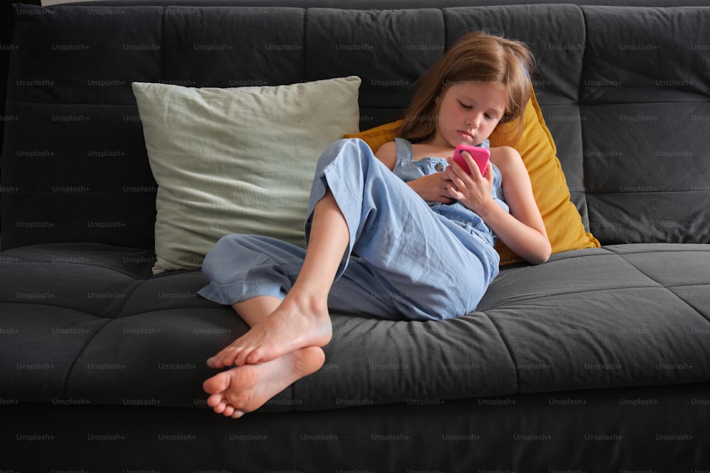 a little girl sitting on a couch holding a cell phone