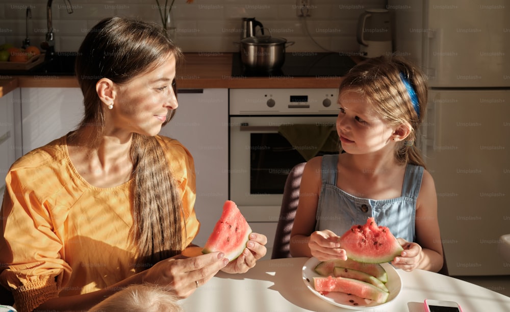 a woman and a girl sitting at a table eating watermelon