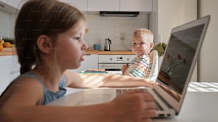 a boy and a girl sitting in front of a laptop computer