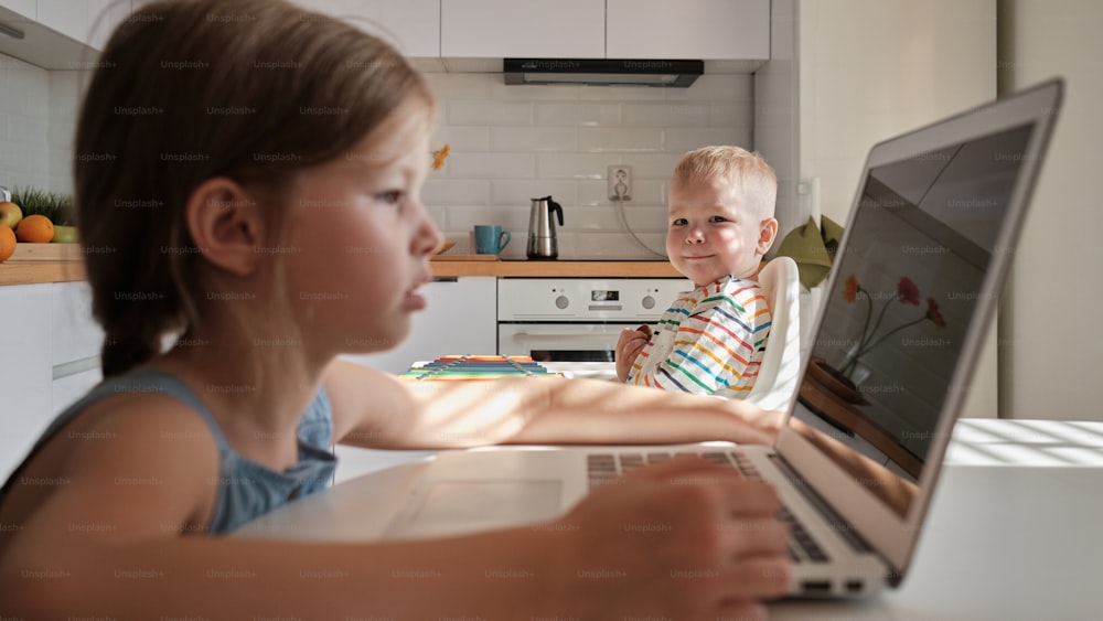 a boy and a girl sitting in front of a laptop computer