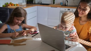 a woman and two children sitting at a table with a laptop
