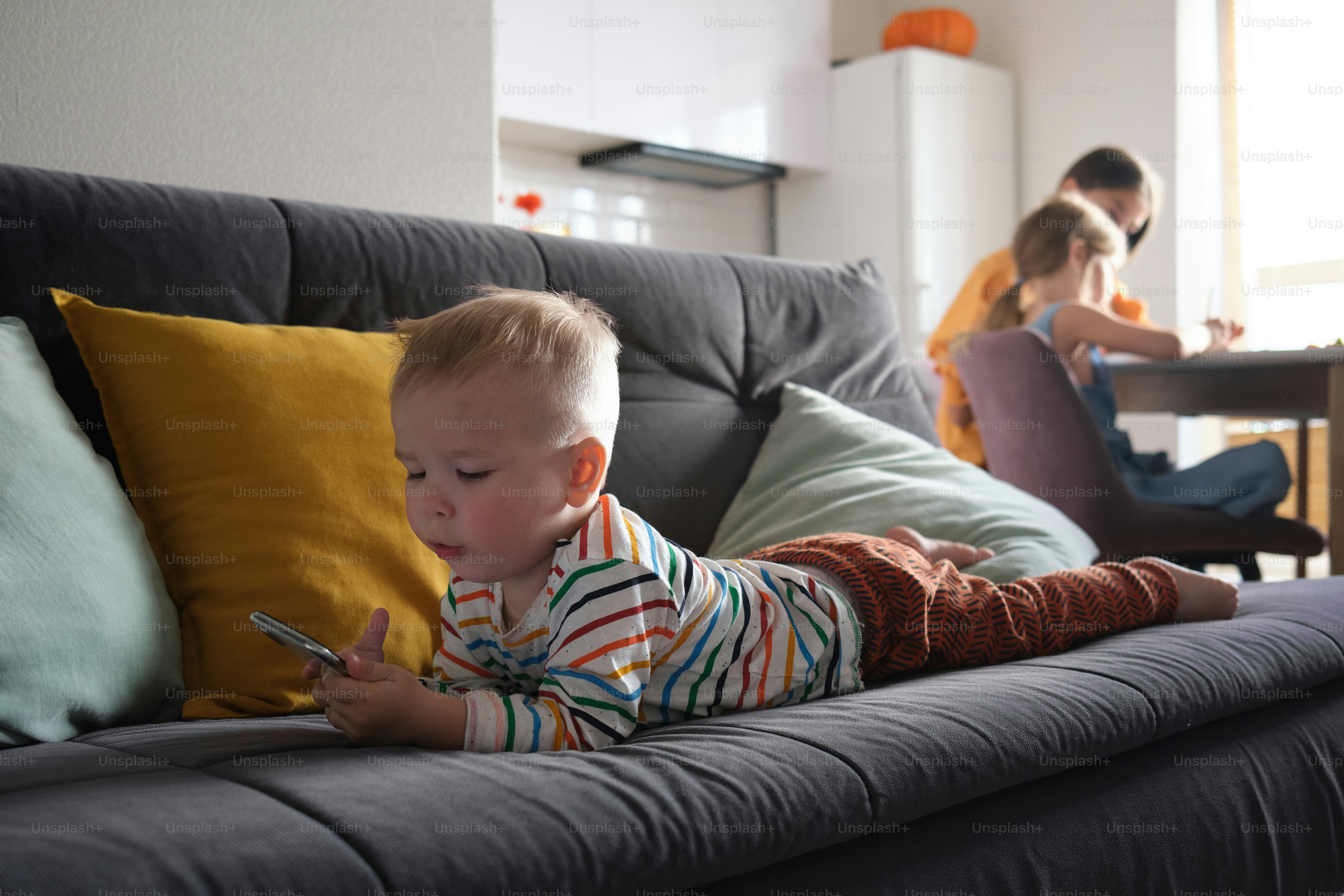 un bambino che si trova su un divano che gioca con un telefono cellulare