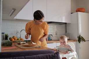 a woman standing over a baby in a high chair