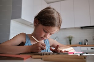 Ein kleines Mädchen, das mit einem Stift und einem Notizbuch an einem Tisch sitzt